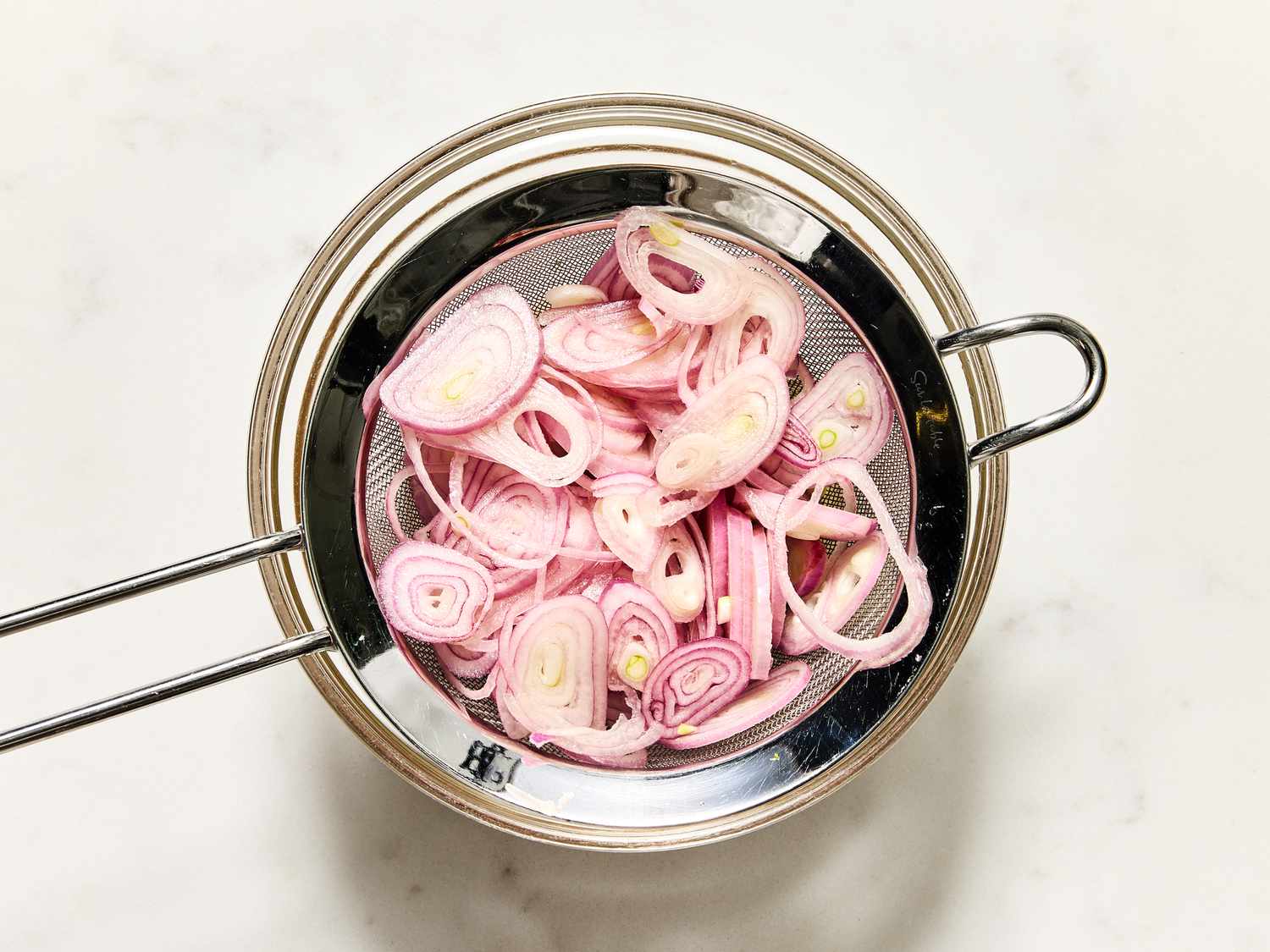 Slices of shallots in a metal strainer with a white background