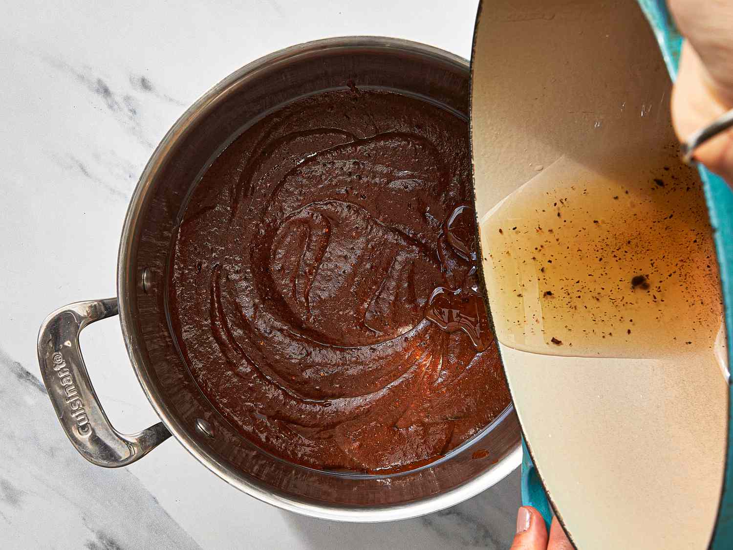 A pot containing a smooth mole sauce, being poured with a liquid from a separate container