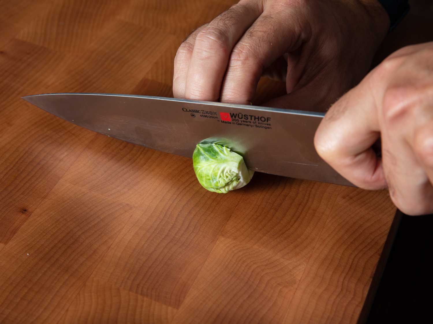 A trimmed Brussels sprout is sliced in half through the stem end with a chef's knife.