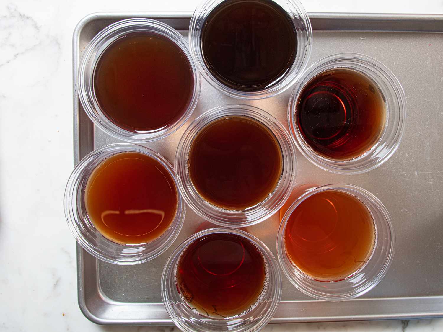 A tray holding seven clear plastic cups filled with varying amounts of tea