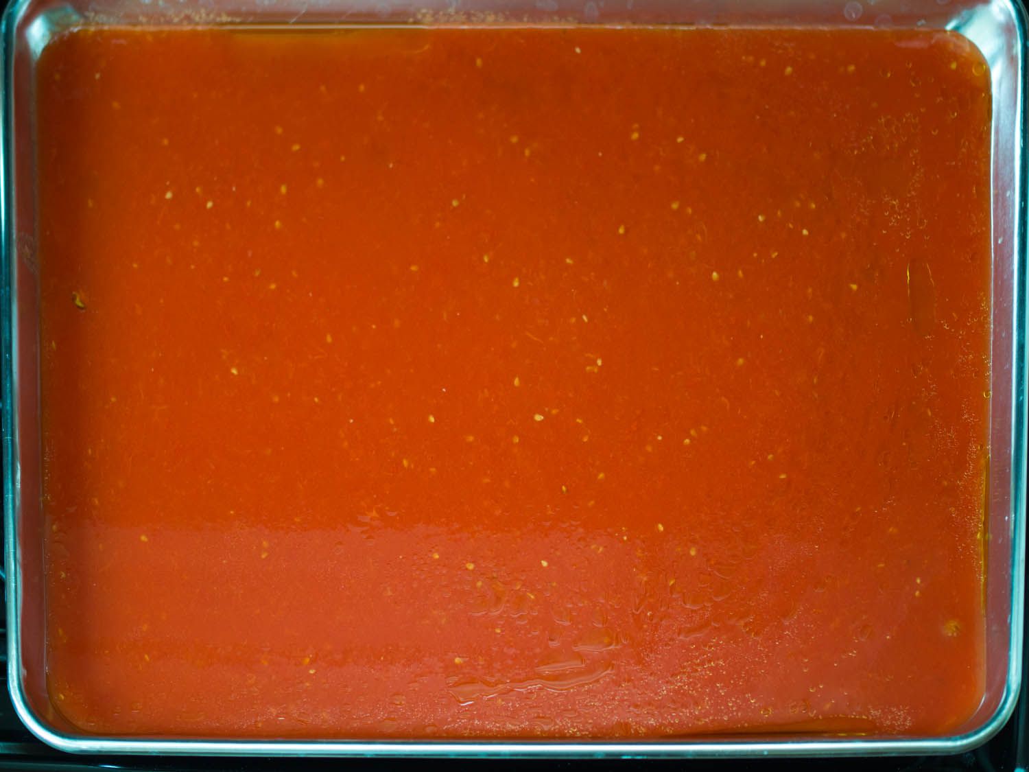 A sheet pan filled with liquid, pureed tomatoes.