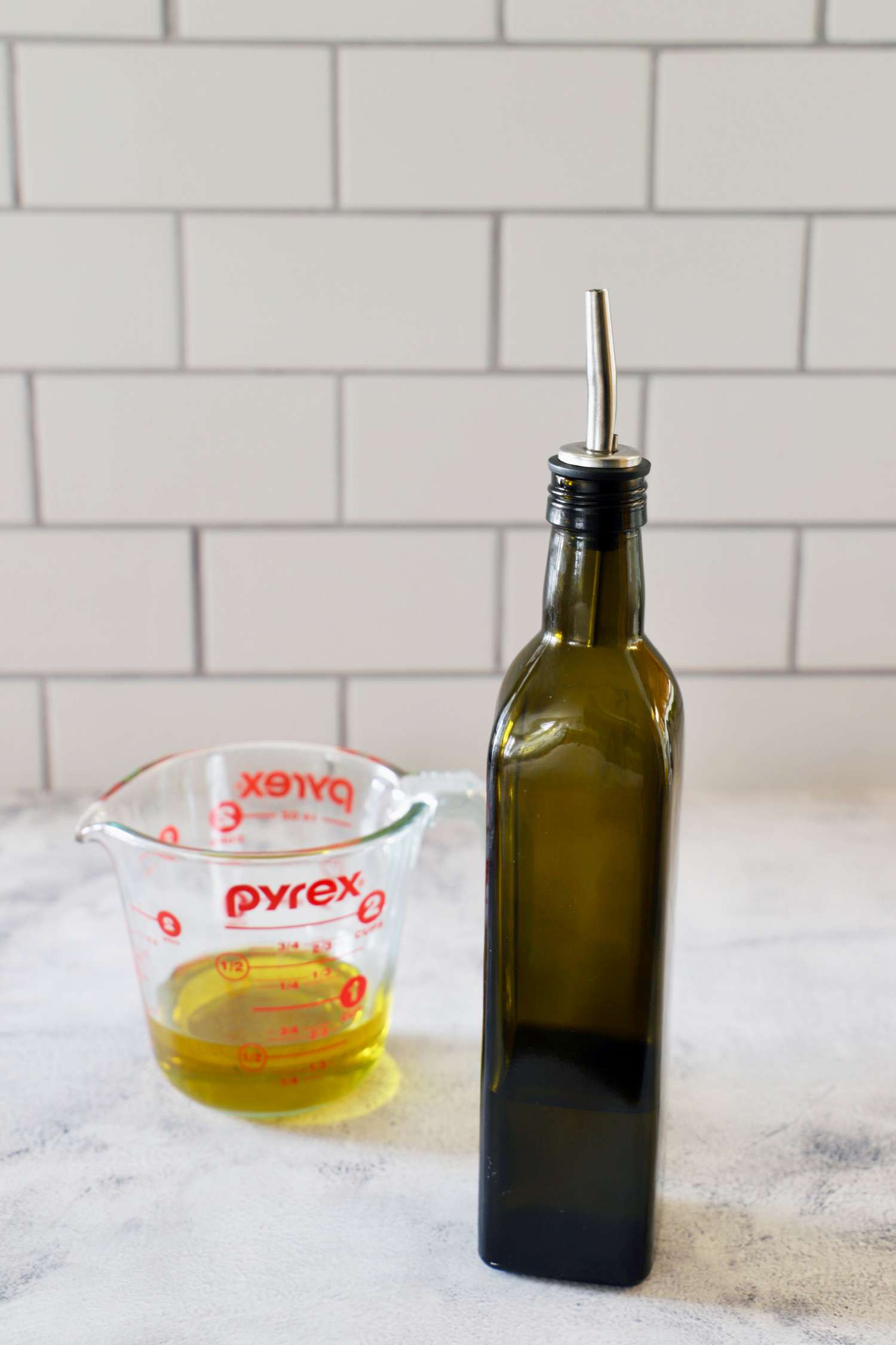 The Zulay oil dispenser next to a cup of olive oil