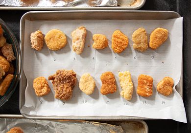 Several chicken nuggets arranged in rows on a baking sheet numbered individually from 1 to 14 for comparison purposes