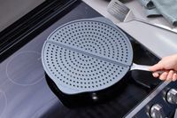 a person holding a pan with the williams sonoma splatter screen on top