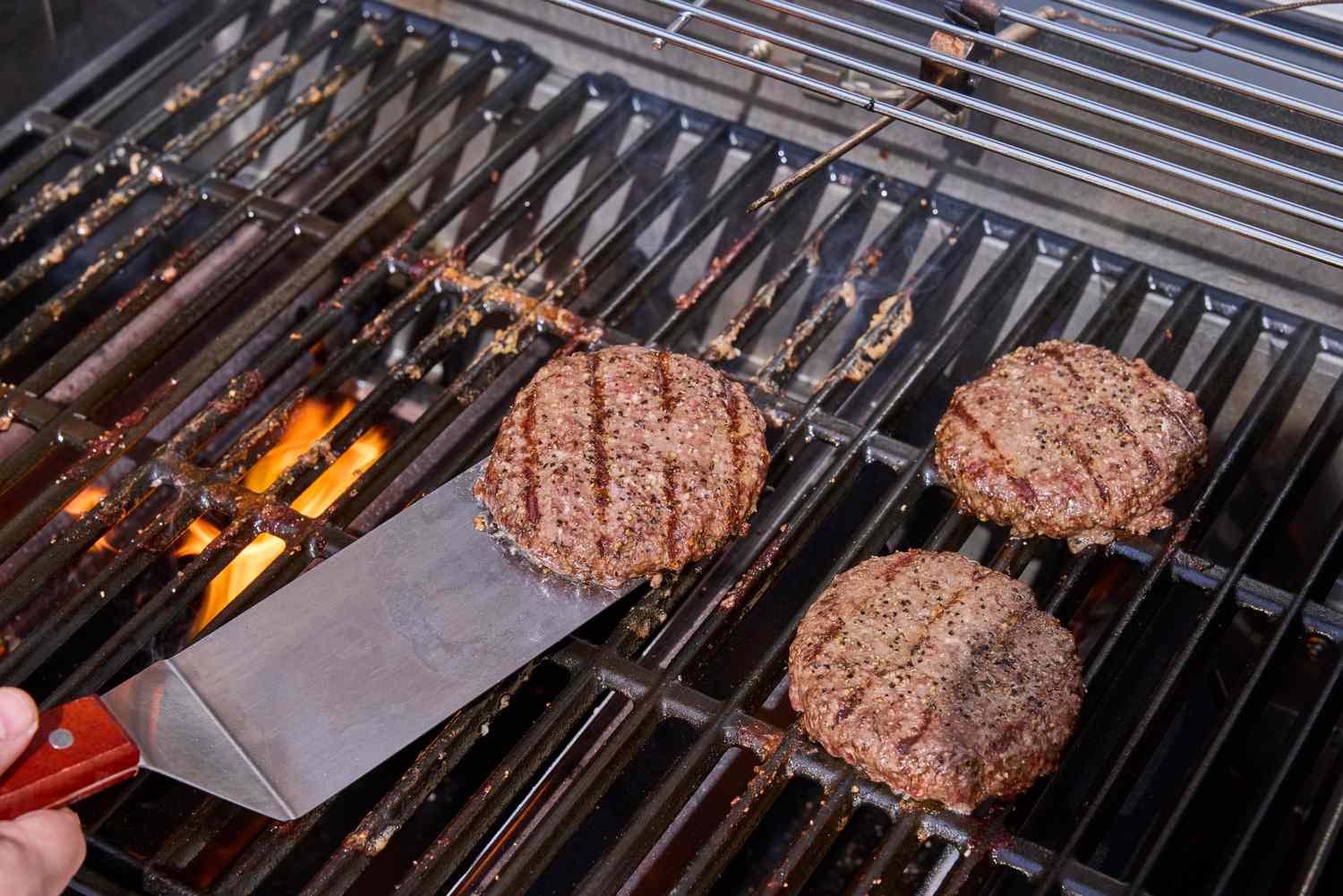 A close-up of a hand sliding a spatula under a patty on the Weber Spirit EP-435 Gas Grill