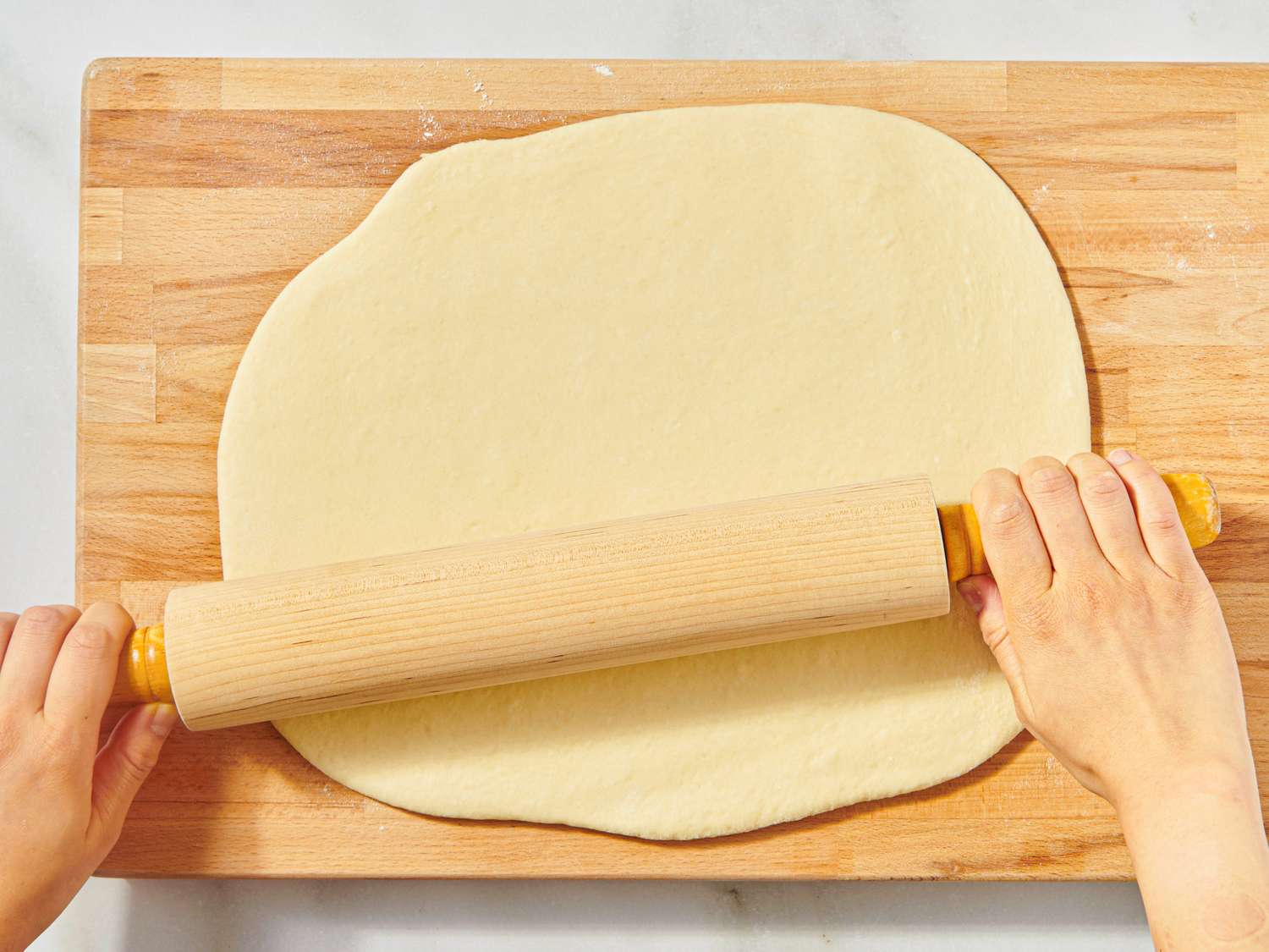 Hands using a rolling pin to flatten dough on a wooden surface
