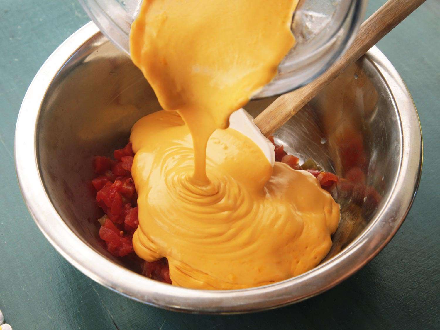 Pouring vegan nacho cheese sauce into a bowl of drained chopped tomatoes and chiles