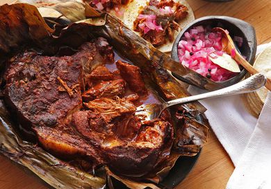 Cochinita Pibil wrapped in banana leaves with pickled diced red onion and tortillas. 