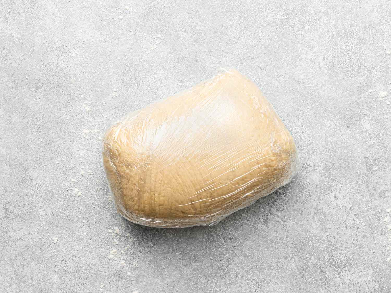 Dough wrapped in plastic wrap, resting on a textured surface.