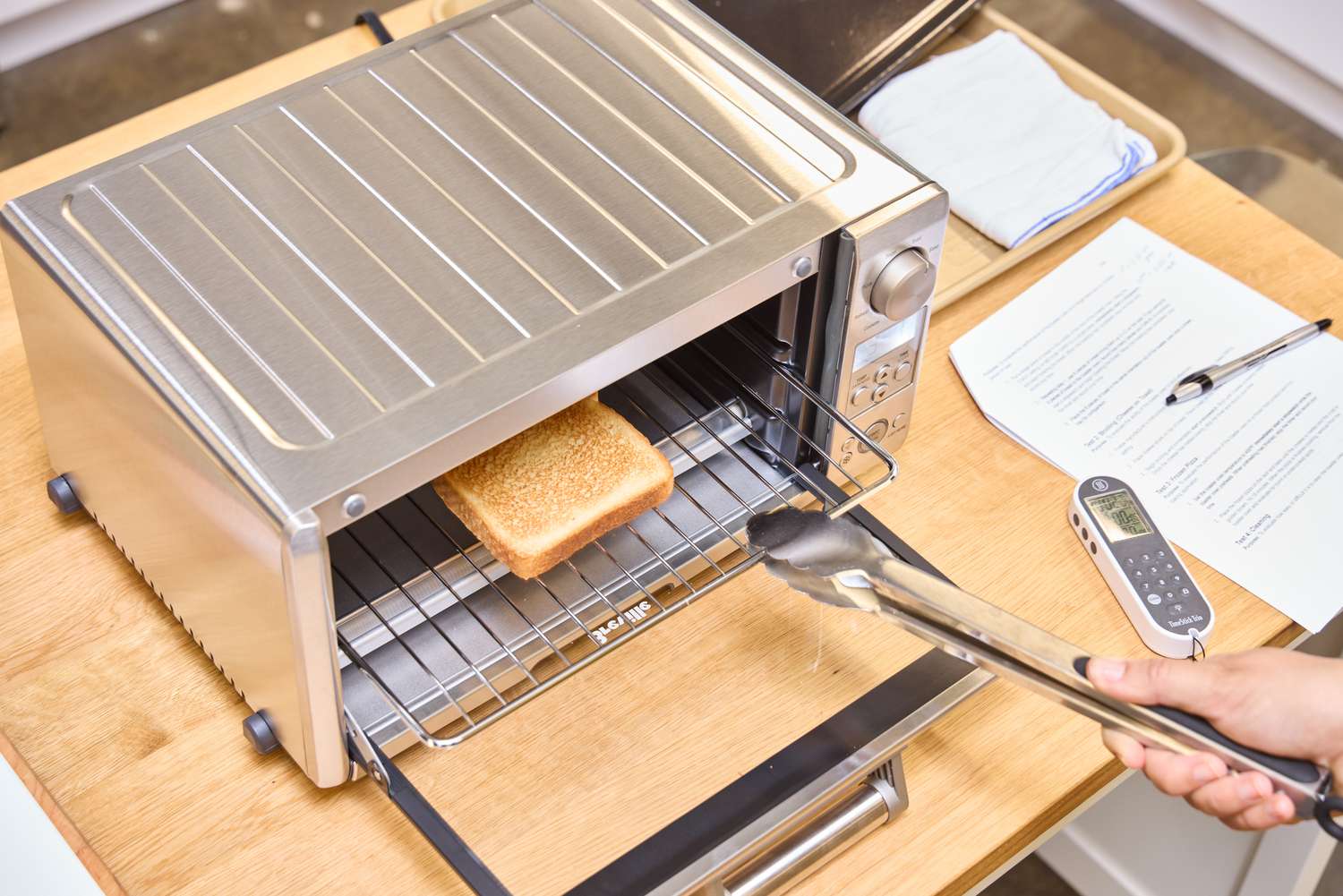 A hand using tongs to move the rack containing bread in side of the Breville the Mini Smart Oven BOV450XL