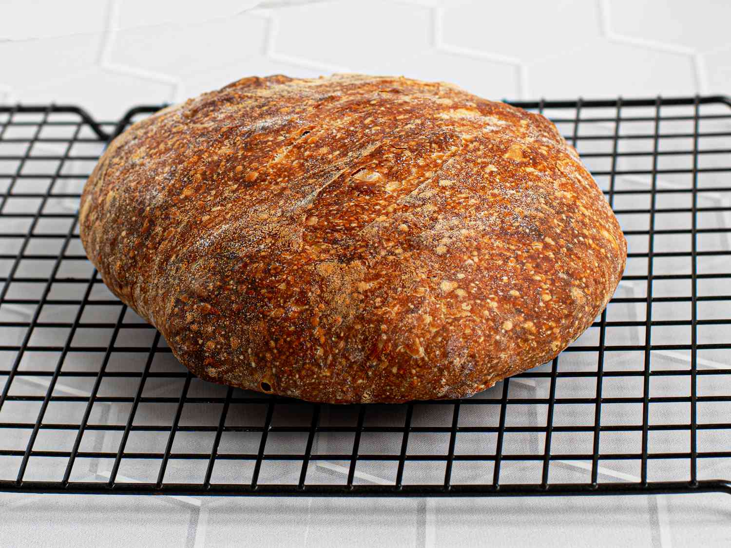 The fully baked loaf of bread placed on a black wire rack over a tiled countertop.
