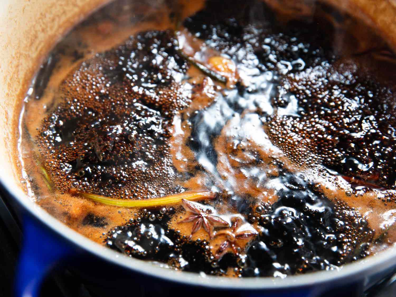 Close-up of the bubbling poaching liquid. Two star anise pods and a stray scallion can be seen bobbing on the surface.