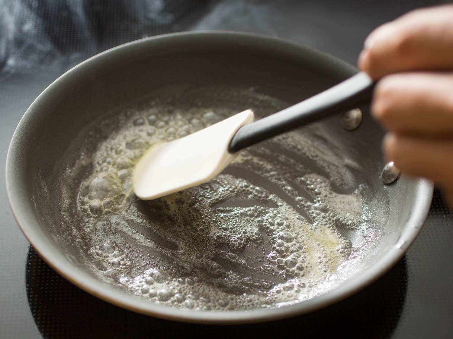 Stirring melted butter with a silicon spatula in a non-stick skillet.