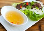 A dish of nuoc cham on a plate containing lettuce, vermicelli and a piece of grilled meat.