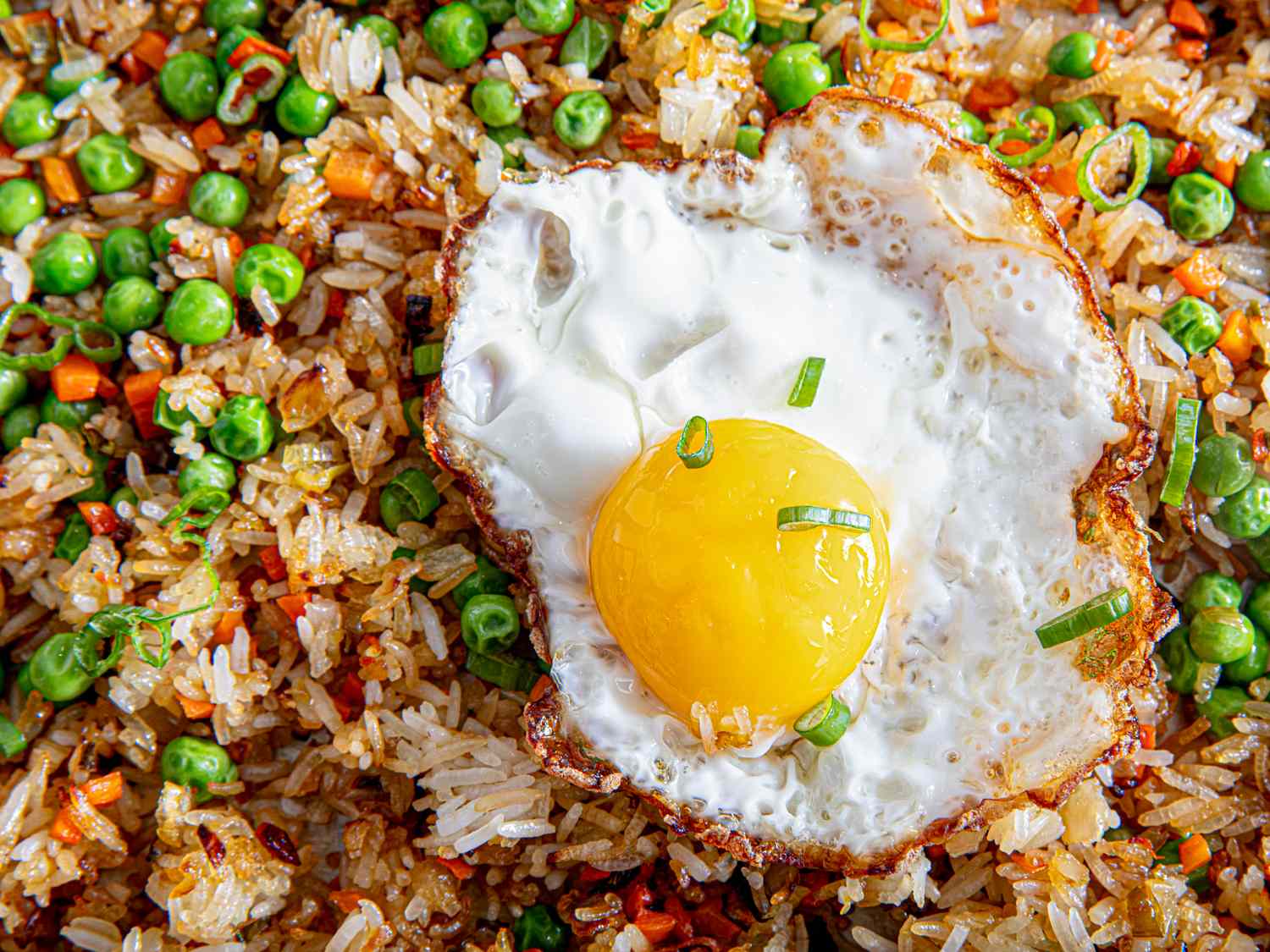 A dish comprising fried rice topped with a sunny side up egg, garnished with peas and green onions