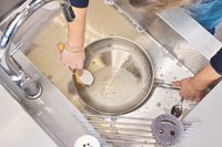 A person washes the All-Clad D3 Stainless-Steel 12-Inch Fry Pan in a sink