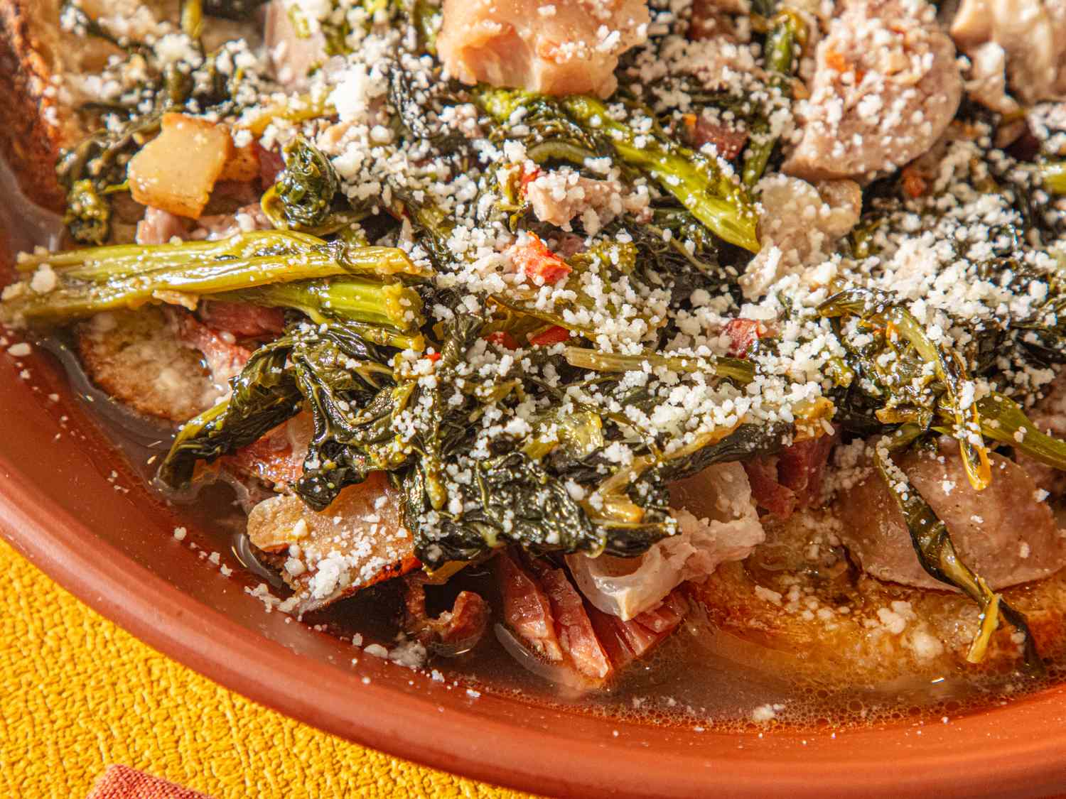 Bowl of Italian wedding soup with greens sausage and grated cheese served in a brown dish