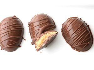 Overhead view of several peanut butter cup eggs, decoratively drizzled with extra chocolate. One of the eggs has been broken in half and upturned to reveal the interior.