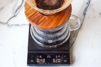 A coffee brewing setup with a wooden dripper on a glass carafe, placed on Hario Polaris Coffee Scale showing readings