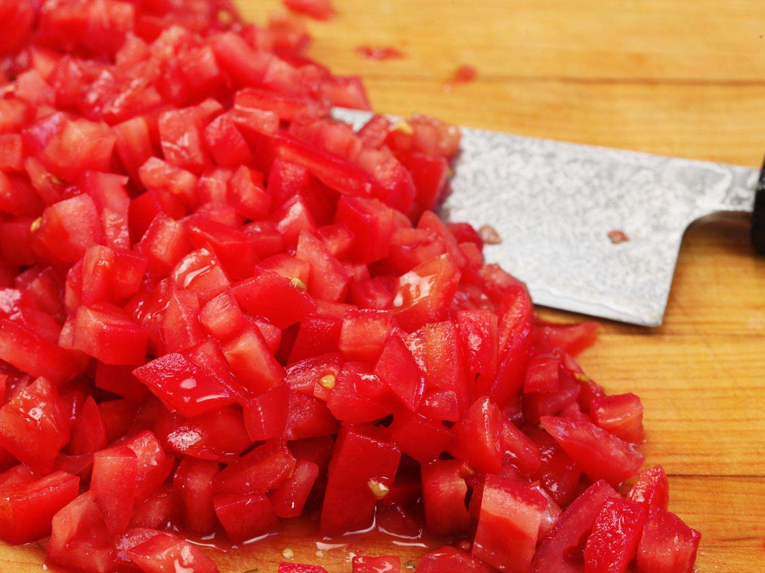 A pile of small pieces of cut tomato on a cutting board with a chef's knife off to the side.