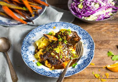 Blue and white bowl of a braised shortrib dinner with bowls of roasted carrots and cabbage in background