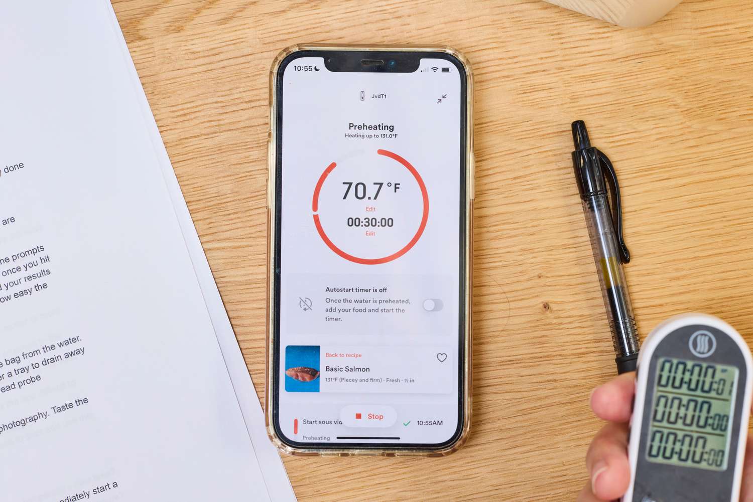 Smartphone displaying the Breville Joule Turbo Sous Vide Machine app interface, surrounded by a pen, paper, and a digital thermometer on a wooden surface
