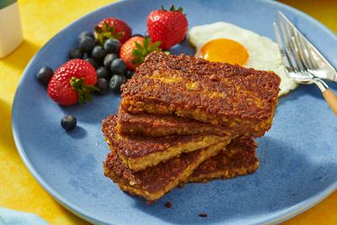 stack of goetta, berries and fried egg on a blue plate. coffee and plate of goetta in the background