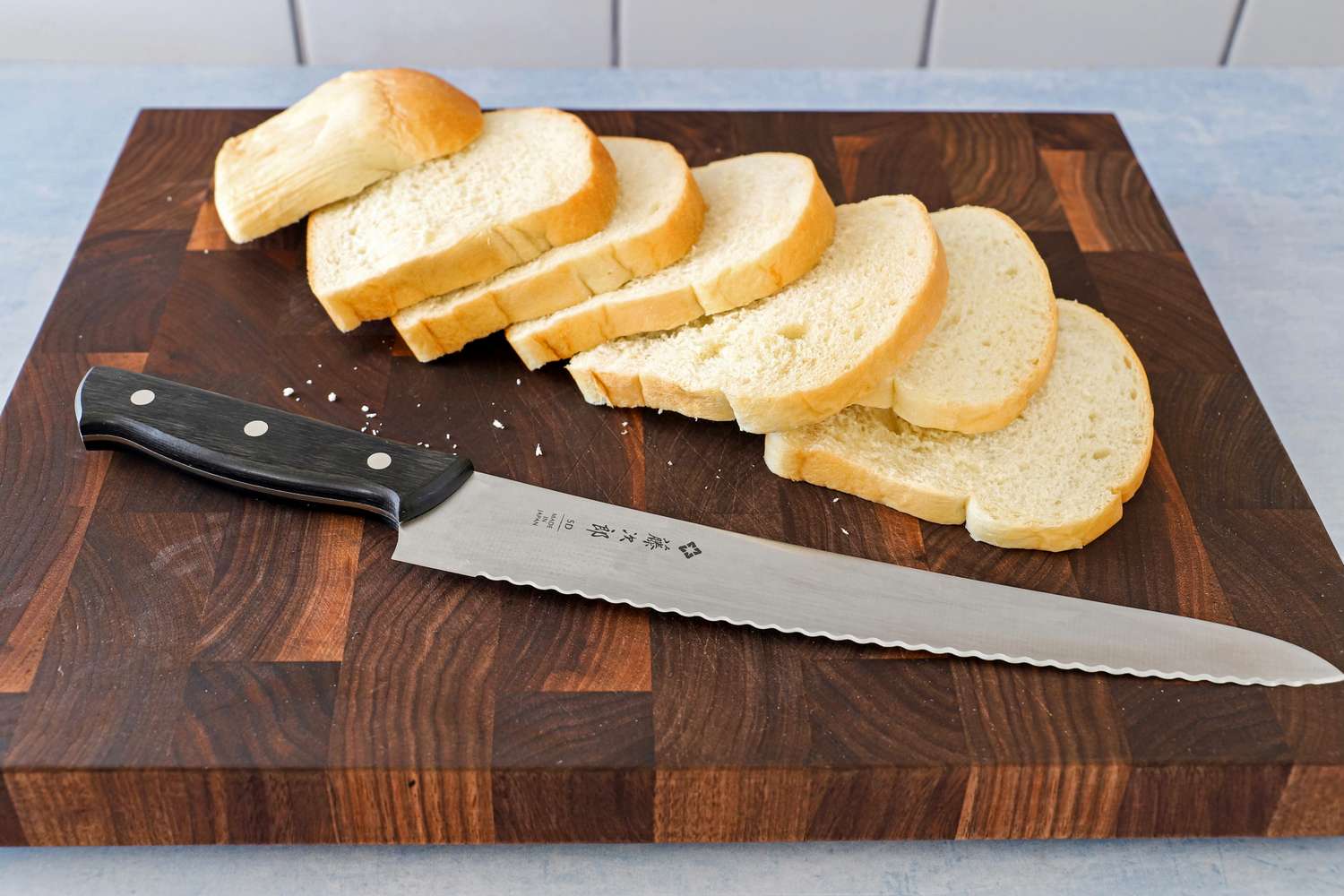 A sliced loaf of bread on a wooden cutting board with a serrated knife placed nearby