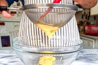 Person straining a mixture into a glass bowl using OXO Good Grips 8-Inch Double Rod Strainer in a kitchen setting