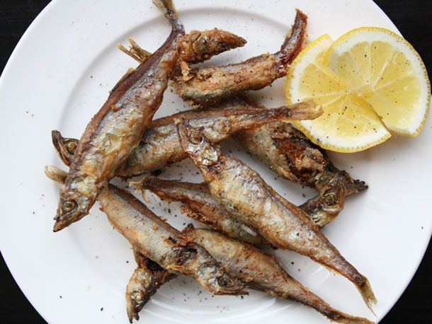 Overhead shot of deep-fried shishamo fish on a white plate, sprinkled with pepper. The plate is garnished with two half-wheels of lemon.