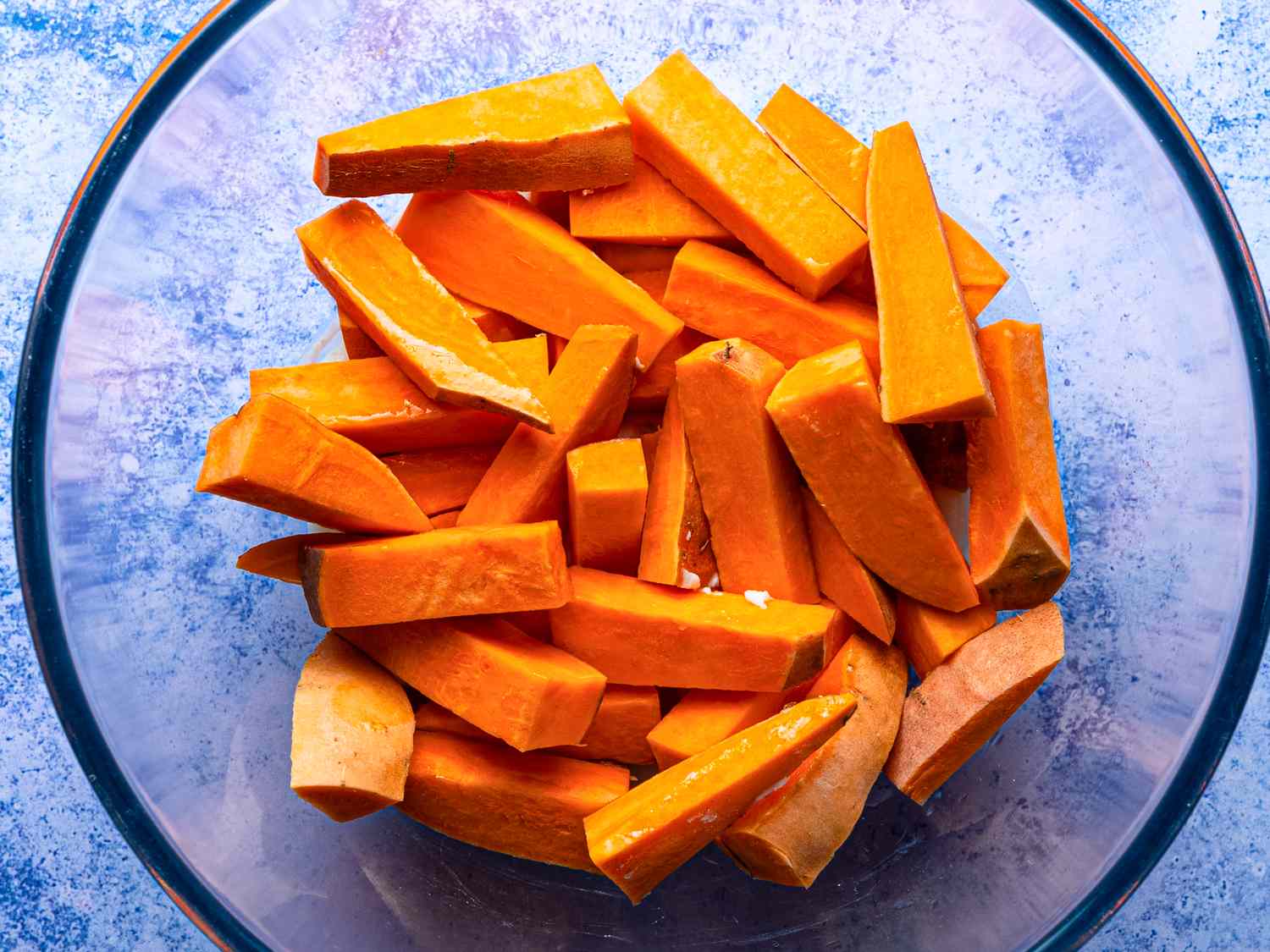 Sweet potato slices in a glass bowl ready for oven frying