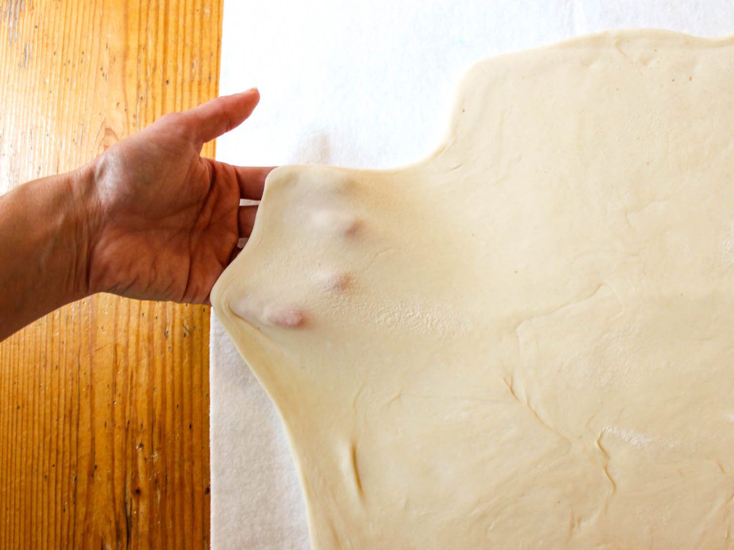 Stretching dough thinly by hand to then layer ingredients on top.