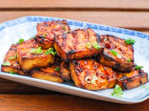 A platter of grilled marinated tofu with chipotle-miso sauce garnished with chopped scallion.