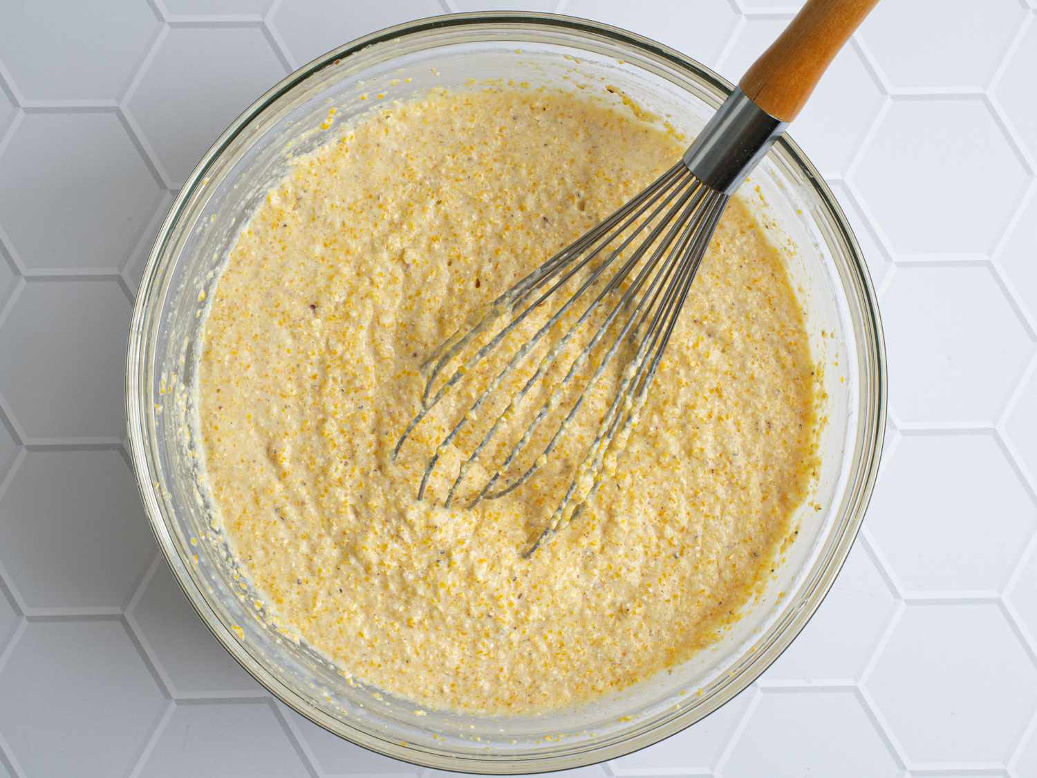  Liquid ingredients whisked into dry ingredient just until thoroughly mixed. There's a whisk inside of the bowl, and the bowl is on top of a white tiled surface.