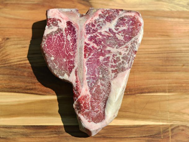 A raw, dry-aged porterhouse steak—well-marbled, with a large layer of fat left at the narrow end, on the strip loin side.