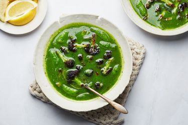 Green Broccoli, leek and snap pea soup from above on a small woven hot pad, with lemons and a second bowl to the side 