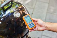 A person checks the temperature gauge on the Weber Smokey Mountain Cooker 18-Inch Charcoal Smoker (721001)