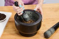 A person using a granite mortar and pestle to crush peppercorns.