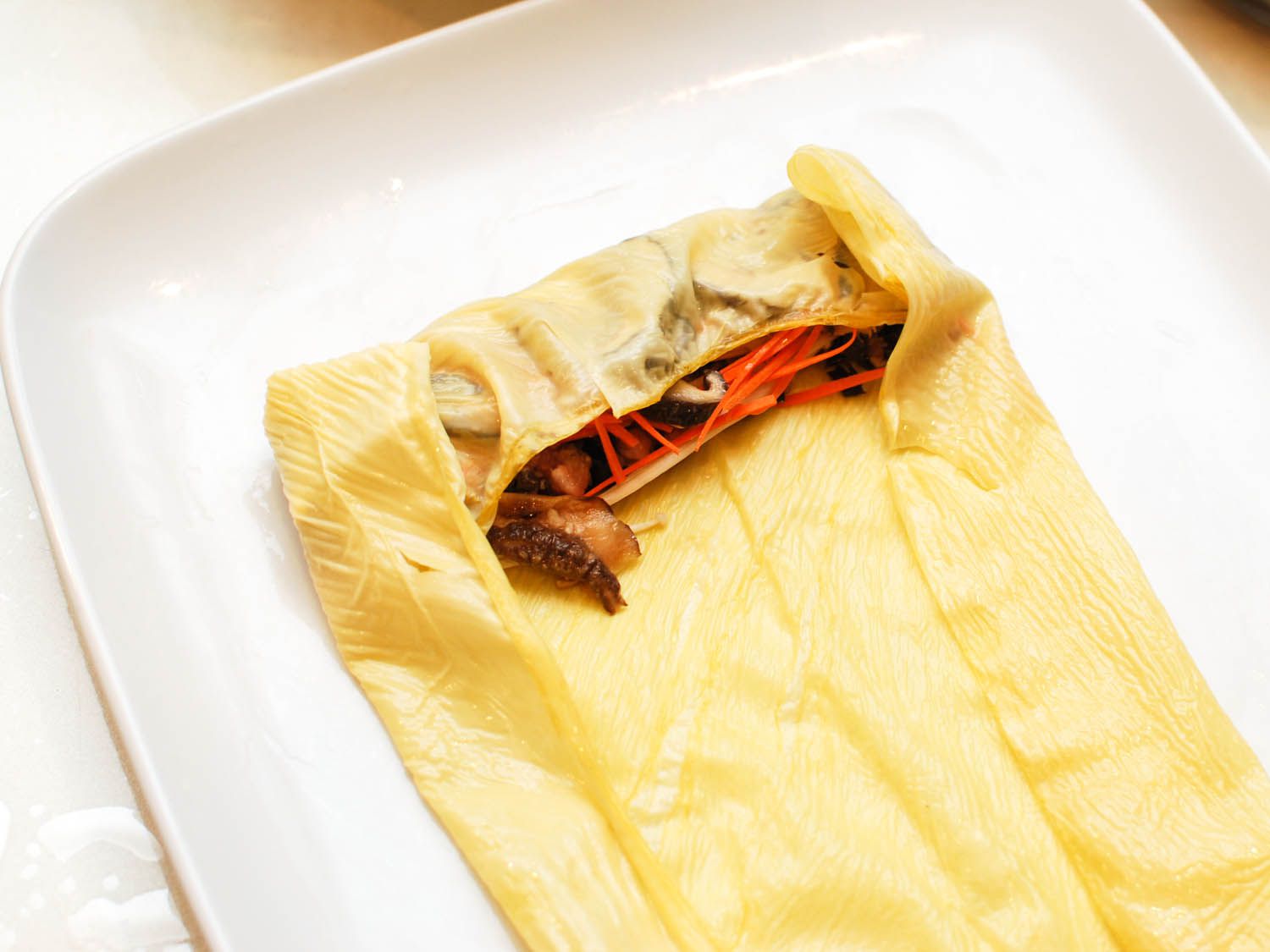 The sides of the bean curd sheet are folded over the ends of the filling mound.