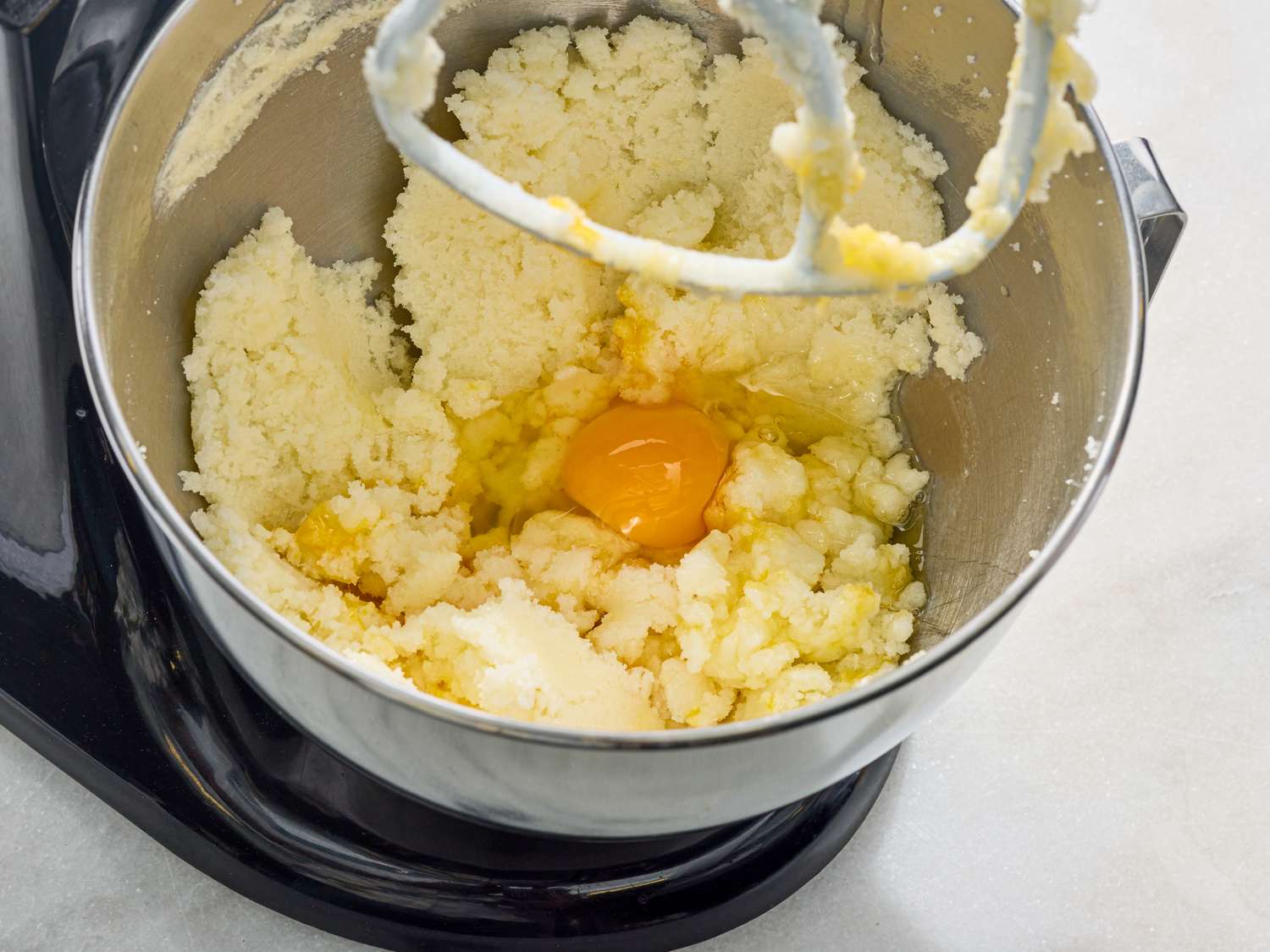 A mixing bowl with cream batter and an egg part of a baking process