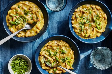 3 blue bowls of chicken, on a chambray textile with 2 glasses of sparking water 