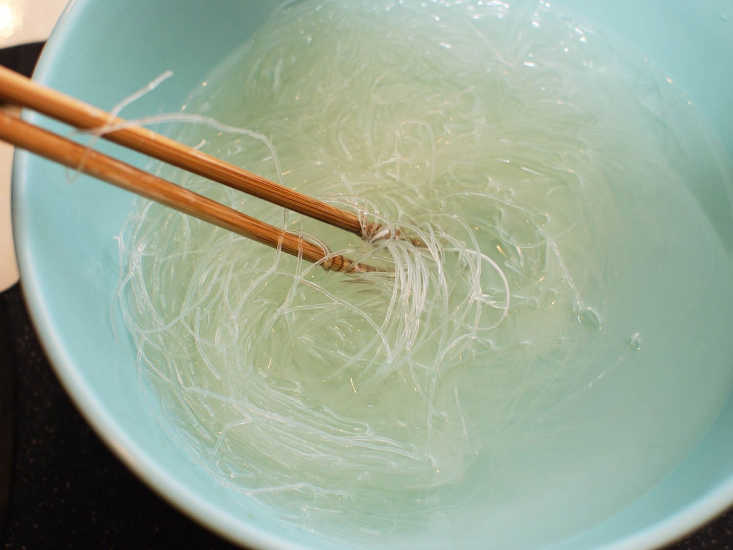 Swirling vermicelli in a bowl of water with chopsticks.