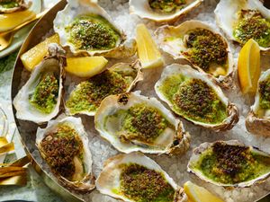 Roasted oysters topped with herbs and seasoning arranged on a platter with lemon wedges