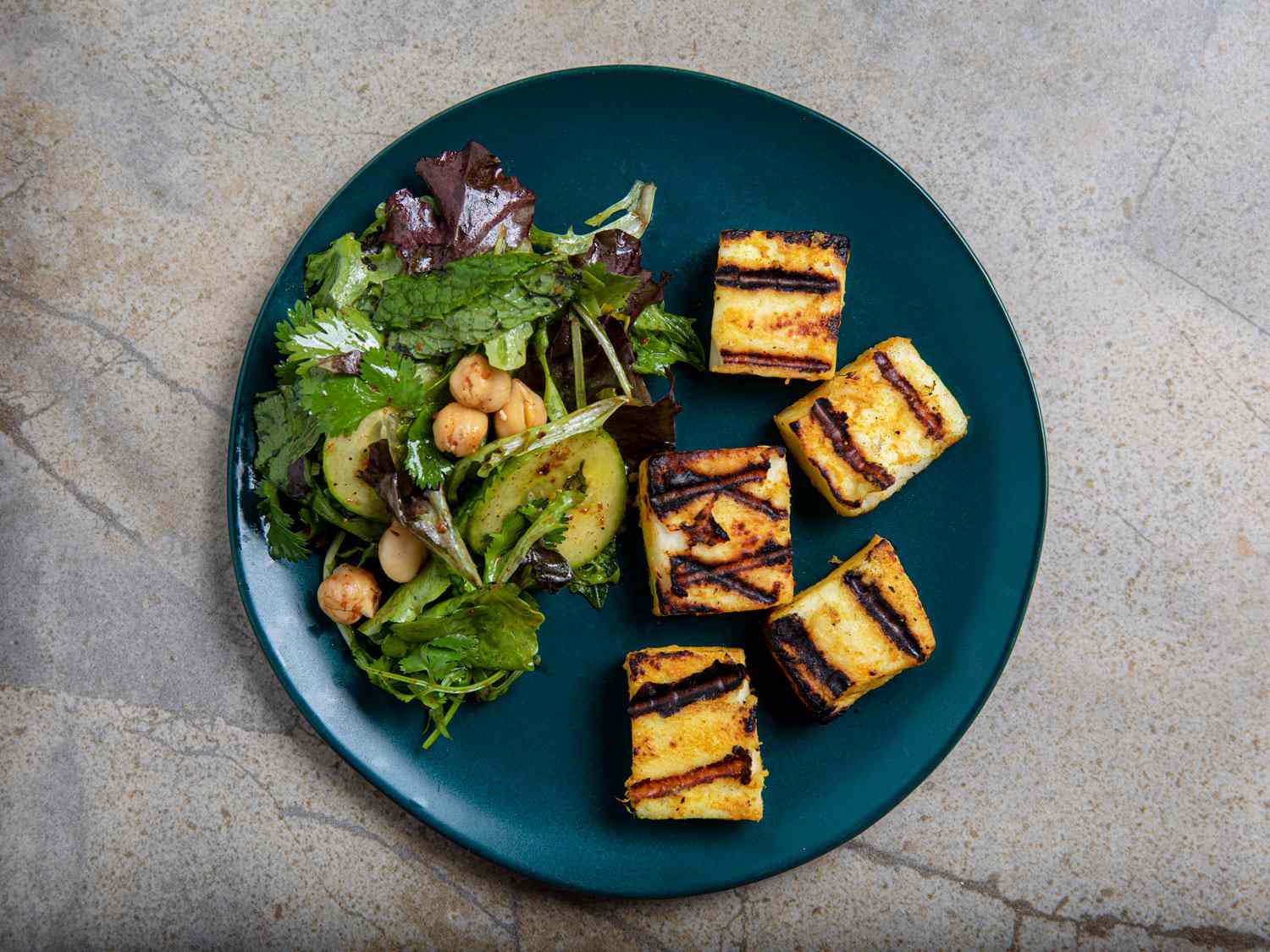 Overhead view of grilled paneer and chickpea salad on a blue plate on a grey marbled backdrop