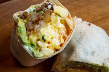 Closeup of a bacon, egg, and cheese breakfast burrito, cut in half and propped up on itself to show off the contents of the burrito to the camera.
