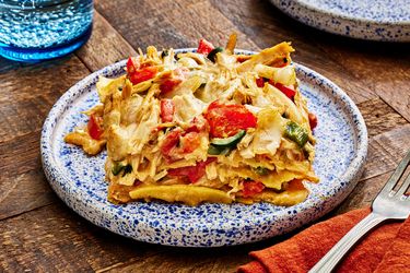 Large serving of King Casserole on a blue splatter plate. The dish is surrounded by a red napkin, a fork and a blue glass of sparkling water