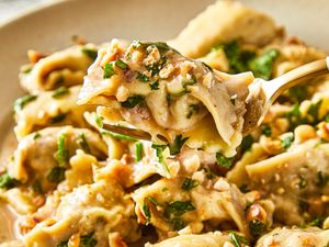 A closeup of a fork lifting a stuffed pasta piece from a dish of agnolotti with garnish