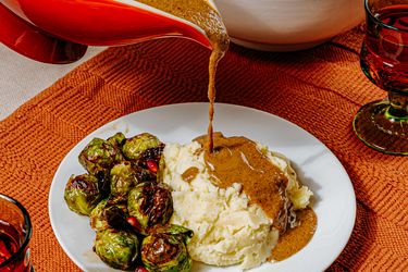 Vegetarian gravy being poured onto mashed potatoes accompanied by roasted Brussels sprouts