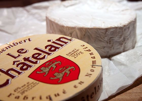A wheel of camembert cheese next to it's wooden packaging.