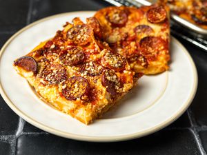 Two square slices of Sicilian pepperoni pizza on a cream colored stoneware plate.